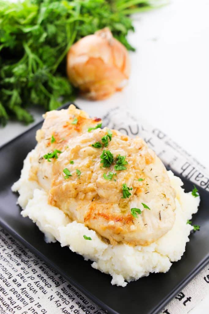 smothered skillet chicken breasts topped with fresh parsley leaves on a bed of mashed potatoes