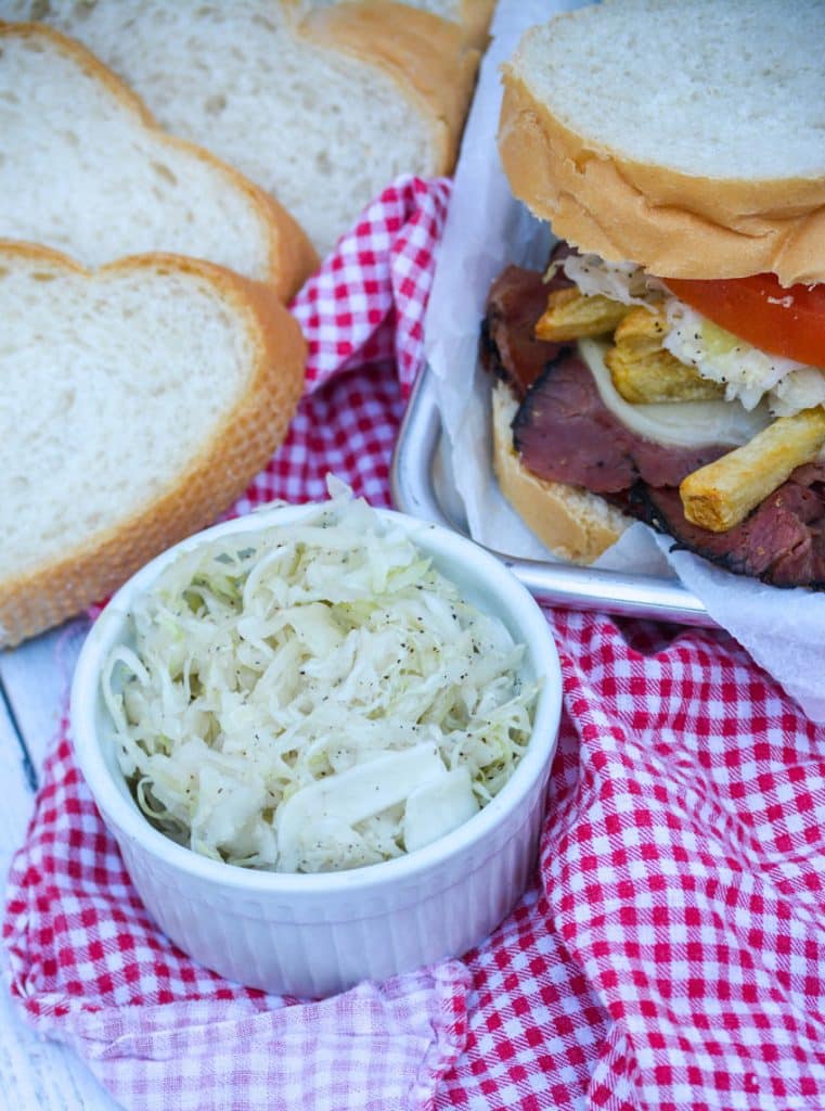 primanti brothers copycat coleslaw in a small white ramekin next to a pastrami sandwich on metal serving tray