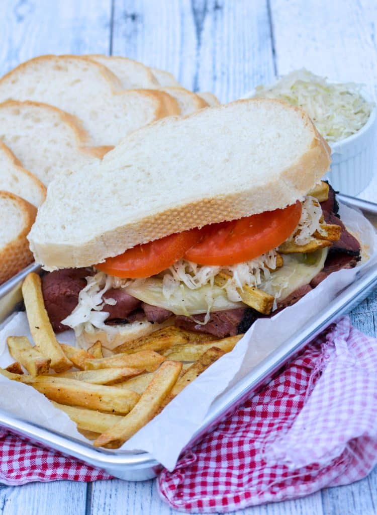 a copycat primanti brothers sandwich on a small metal tray surrounded by cooked french fries