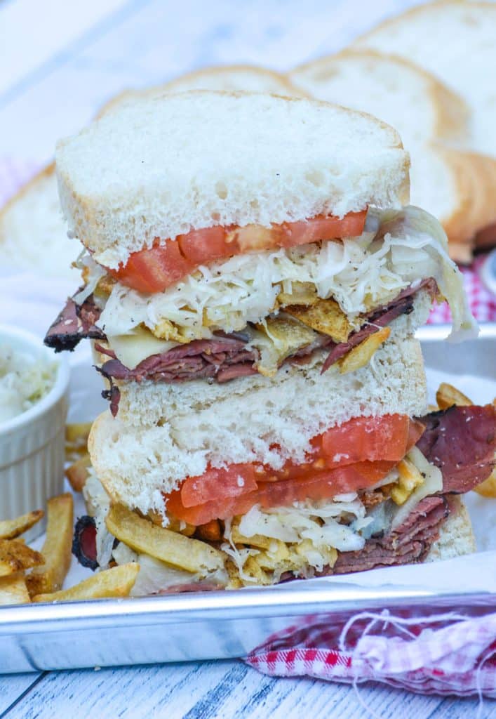 two halves of a copycat primanti bros sandwich stacked on top of each other to show the filling inside; served on a small metal tray