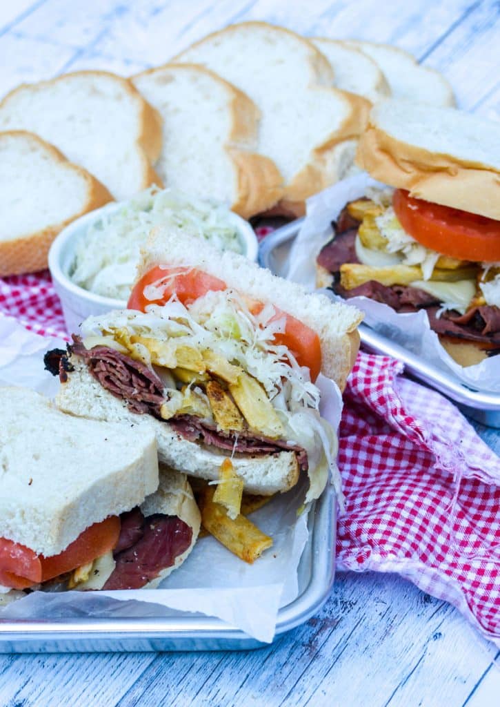 copycat primanti brothers sandwich cut in half and shown on a metal serving tray with bowl of coleslaw in the background