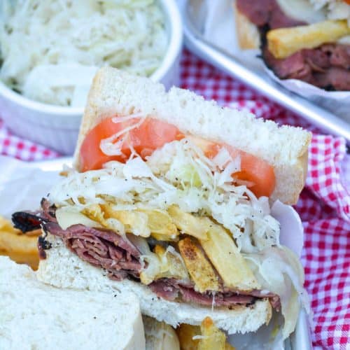 copycat primanti brothers sandwich cut in half and shown on a metal serving tray with bowl of coleslaw in the background