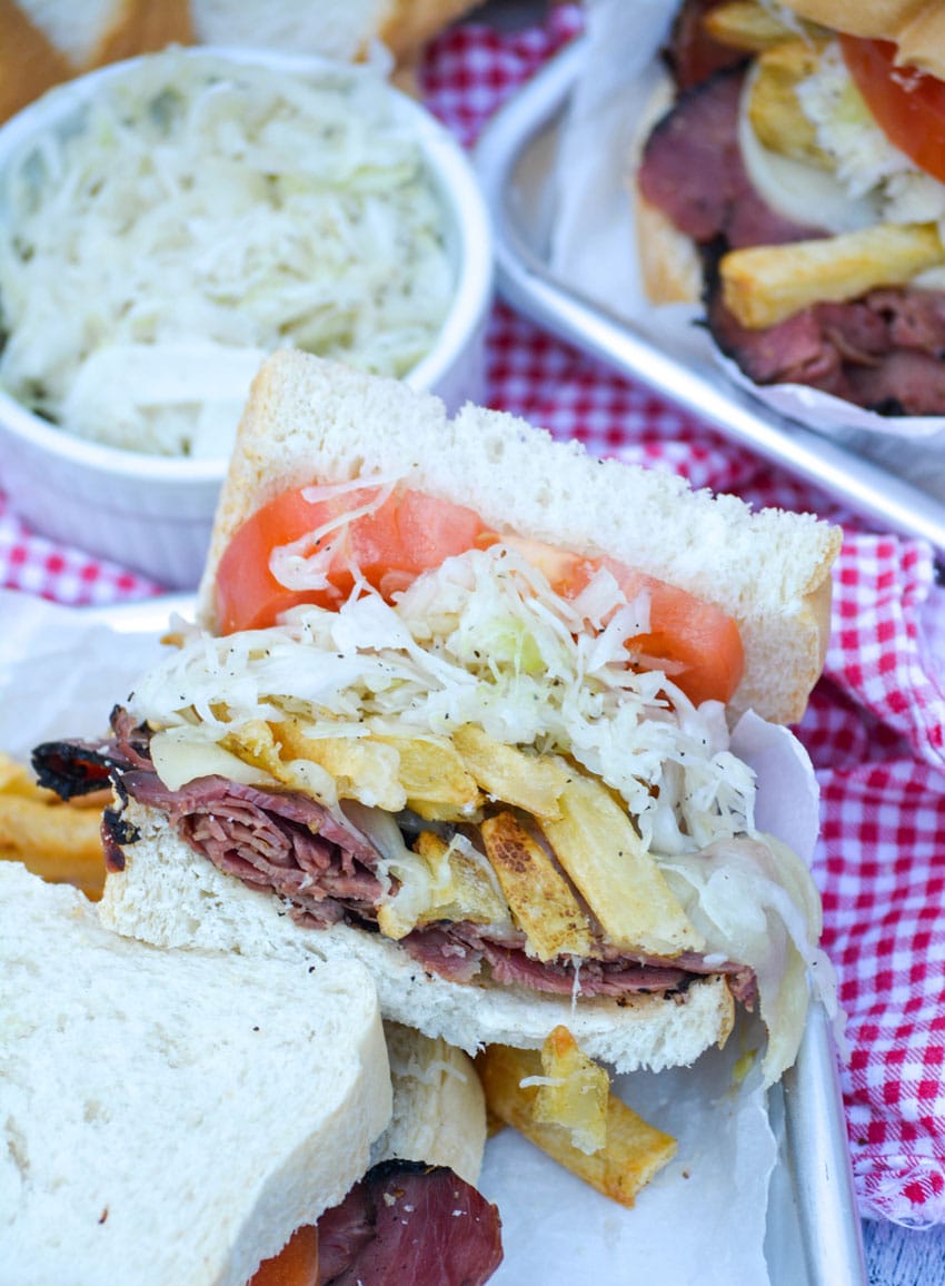 copycat primanti brothers sandwich cut in half and shown on a metal serving tray with bowl of coleslaw in the background