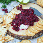 cranberry salsa spread over a softened block of cream cheese on a wooden cutting board surrounded by crackers