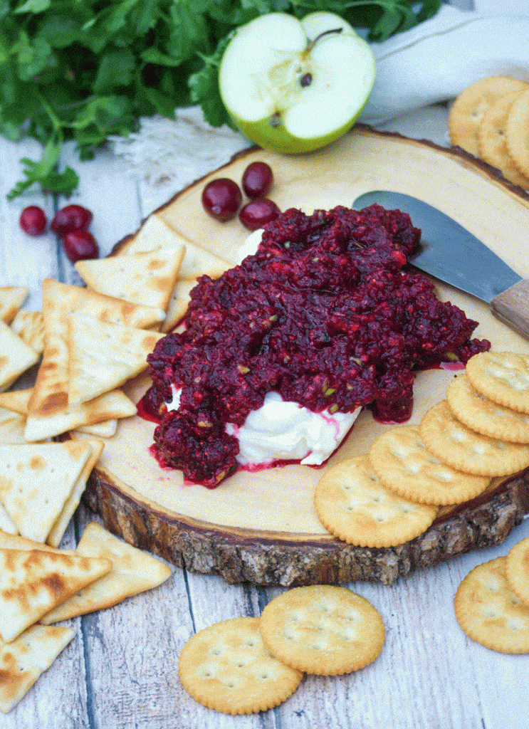 cranberry salsa spread over a softened block of cream cheese on a wooden cutting board surrounded by crackers
