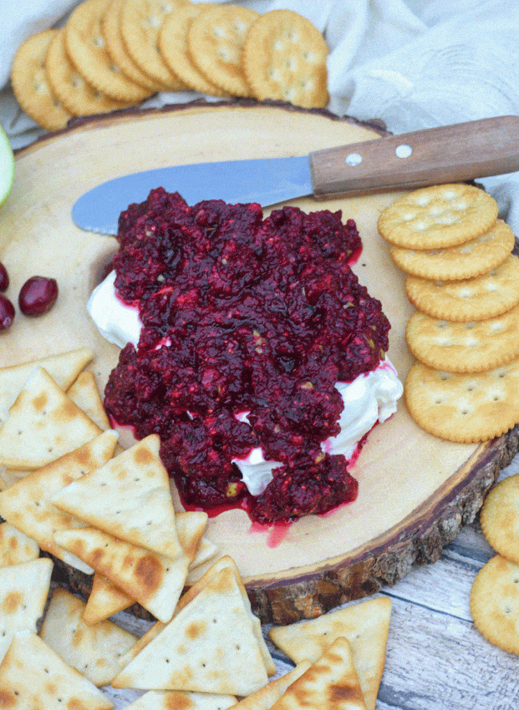 cranberry salsa spread over a softened block of cream cheese on a wooden cutting board surrounded by crackers