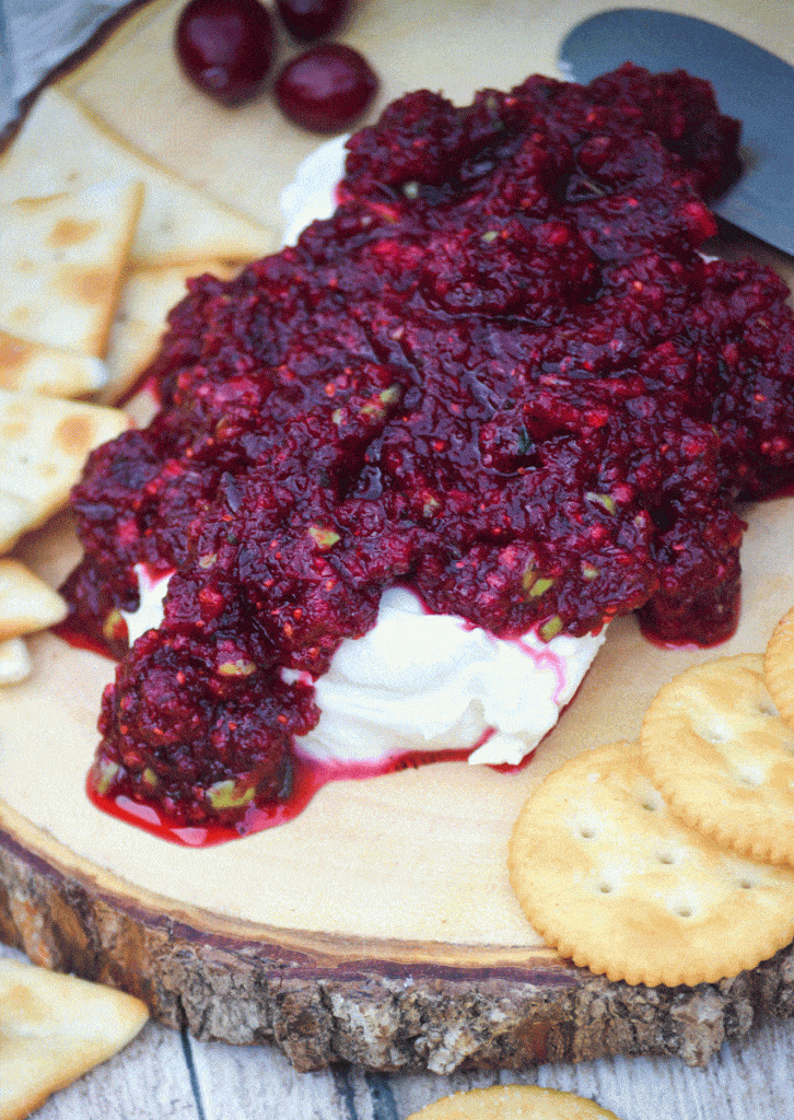 cranberry salsa spread over a softened block of cream cheese on a wooden cutting board surrounded by crackers