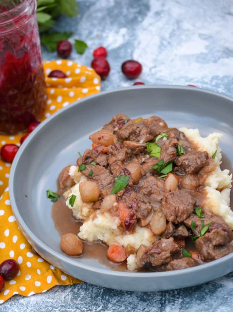 cranberry beef stew over mashed potatoes in large shallow gray bowls