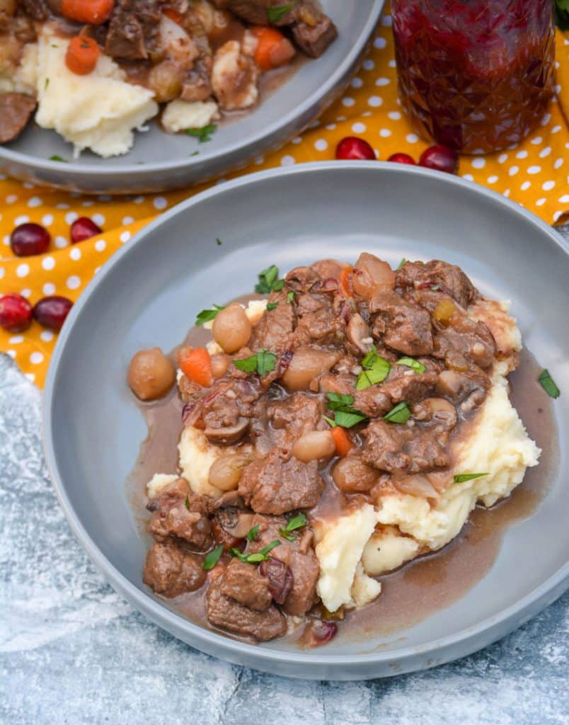 cranberry beef stew over mashed potatoes in large shallow gray bowls