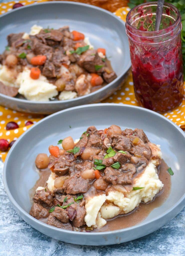cranberry beef stew over mashed potatoes in large shallow gray bowls