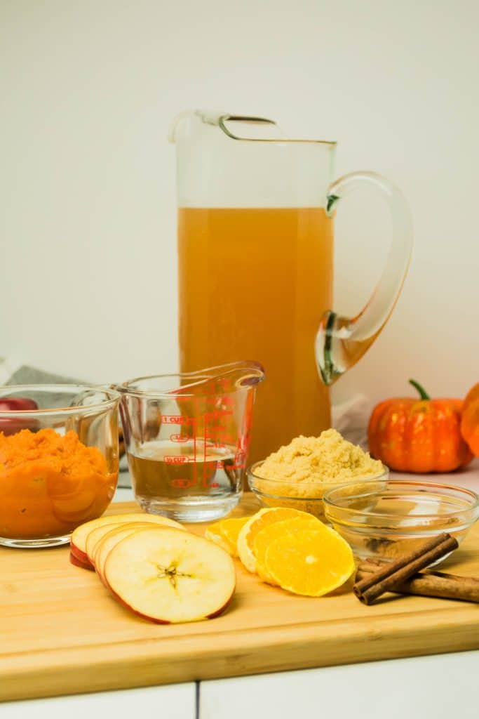 ingredients needed to make a batch of spiced cider with pumpkin spread out on a wooden cutting board