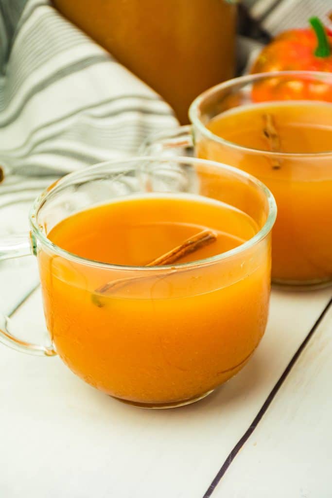 spiced cider with pumpkin in a glass mug with a cinnamon stick floating in the drink