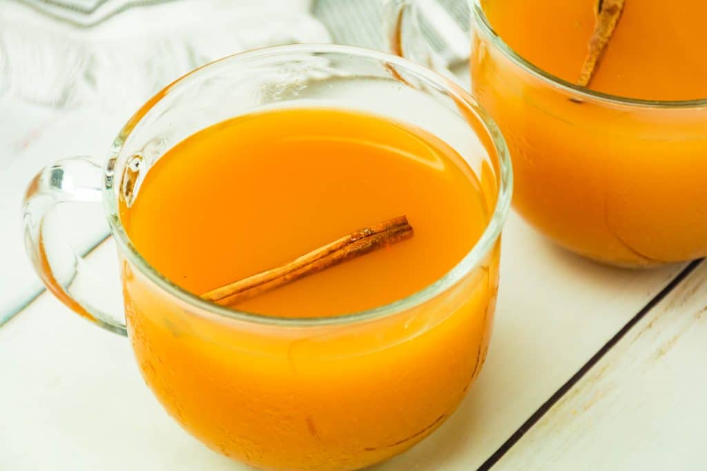 spiced cider with pumpkin in a glass mug with a cinnamon stick floating in the drink