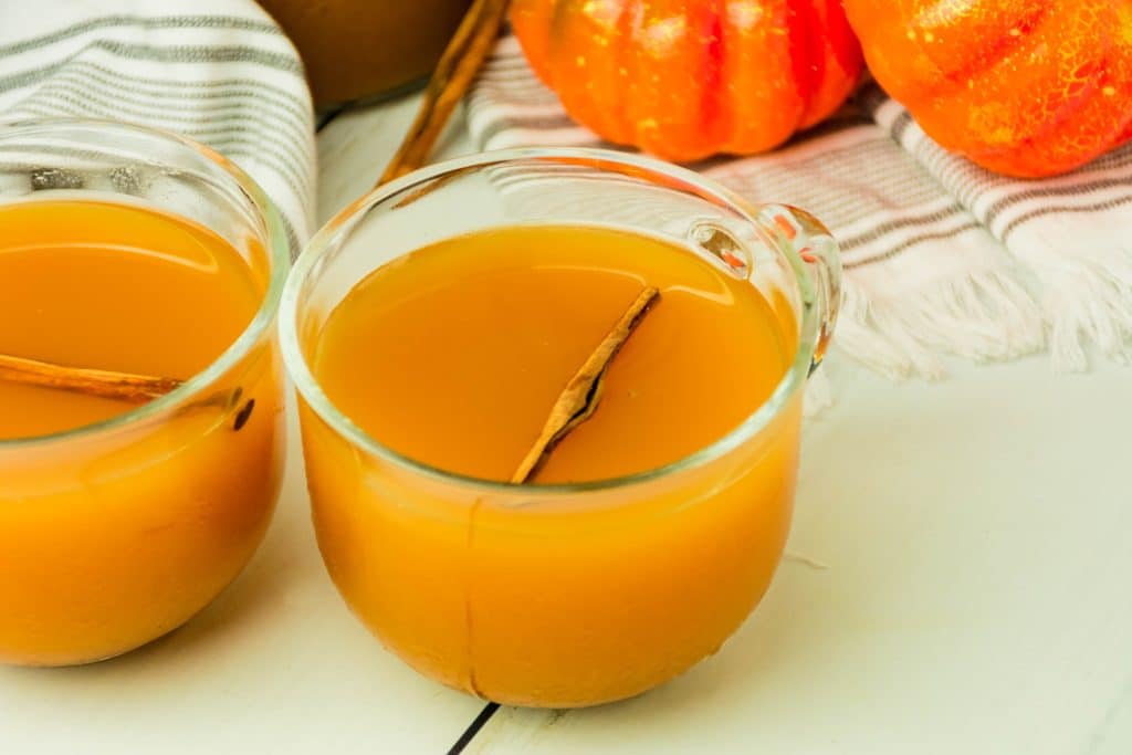 spiced cider with pumpkin in a glass mug with a cinnamon stick floating in the drink