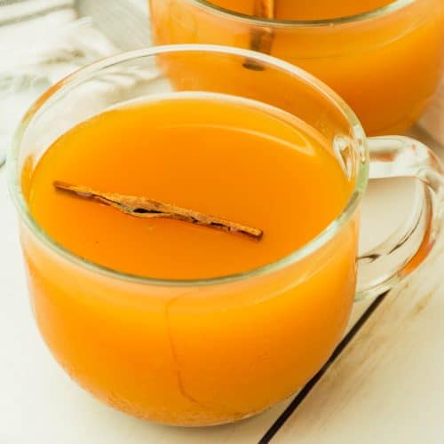 spiced cider with pumpkin in a glass mug with a cinnamon stick floating in the drink