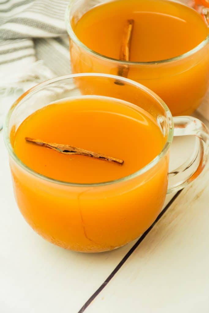 spiced cider with pumpkin in a glass mug with a cinnamon stick floating in the drink