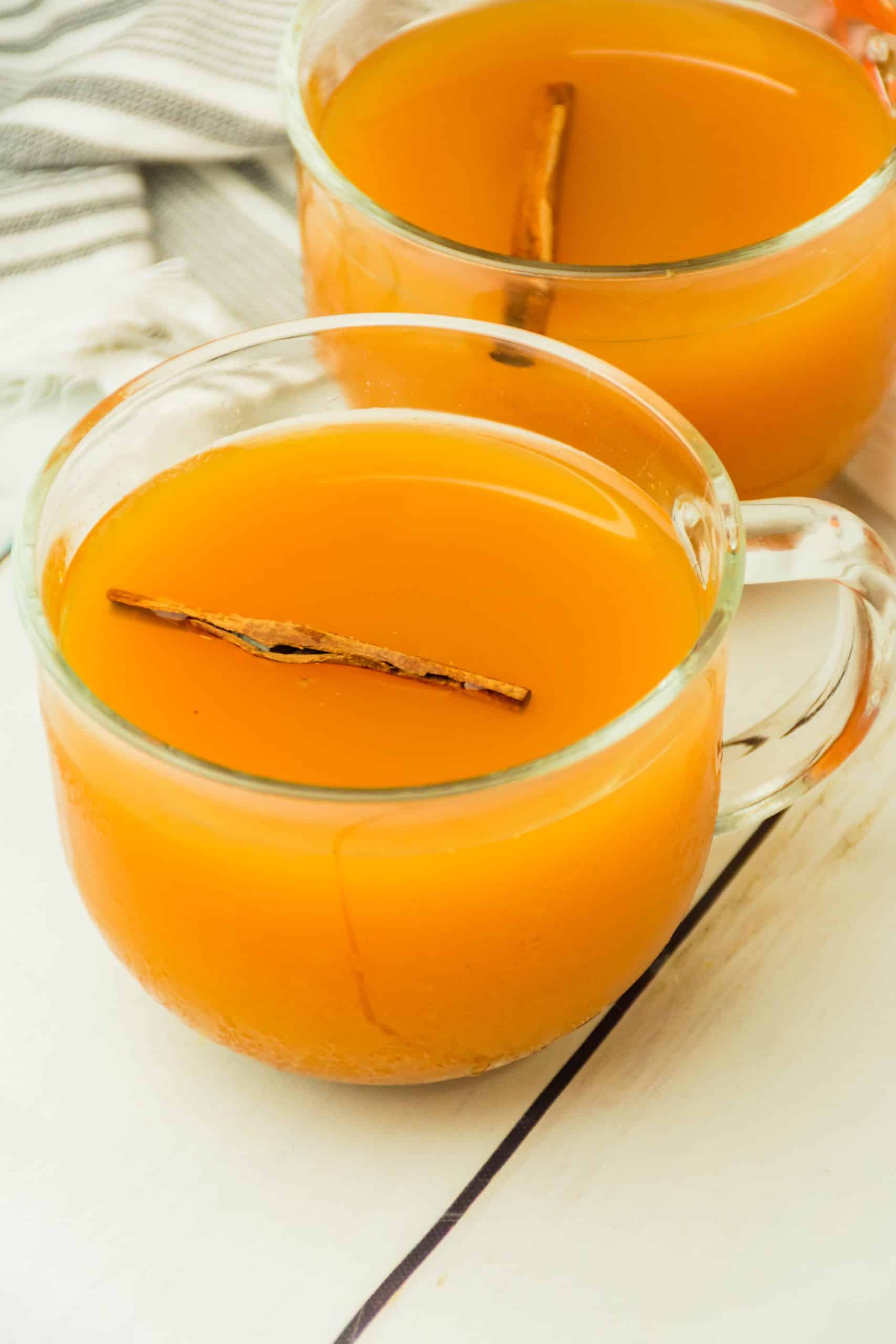 spiced cider with pumpkin in a glass mug with a cinnamon stick floating in the drink