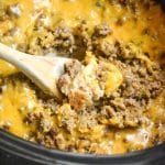 a wooden spoon scooping slow cooker cheeseburger casserole from a black crock