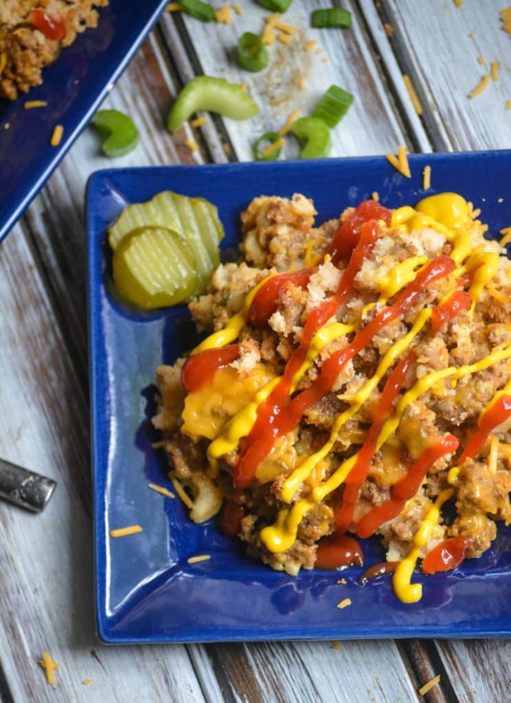 slow cooker cheeseburger casserole on a small square blue plate with a drizzle of ketchup & mustard