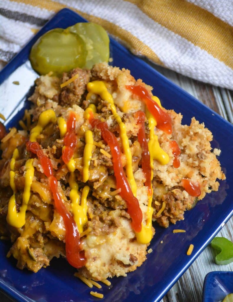 slow cooker cheeseburger casserole on a small square blue plate with a drizzle of ketchup & mustard
