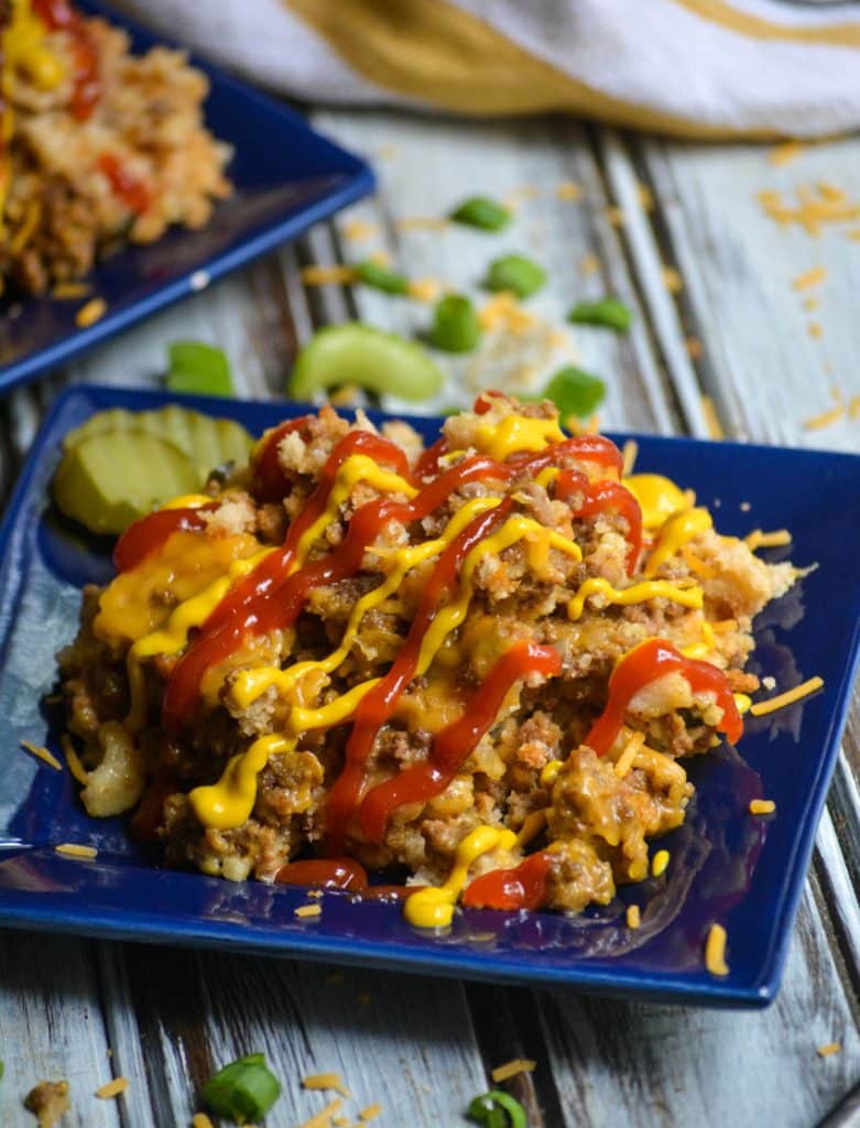 slow cooker cheeseburger casserole on a small square blue plate with a drizzle of ketchup & mustard