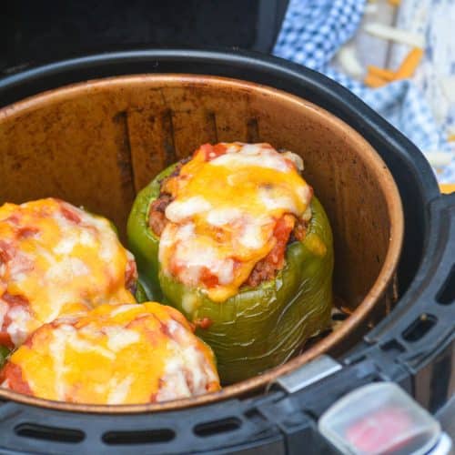 three cheese topped stuffed green peppers in the basket of an air fryer