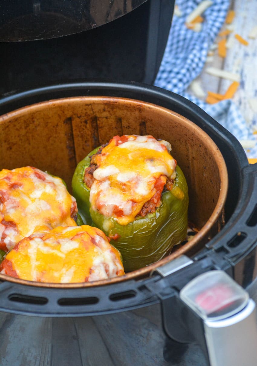 three cheese topped stuffed green peppers in the basket of an air fryer