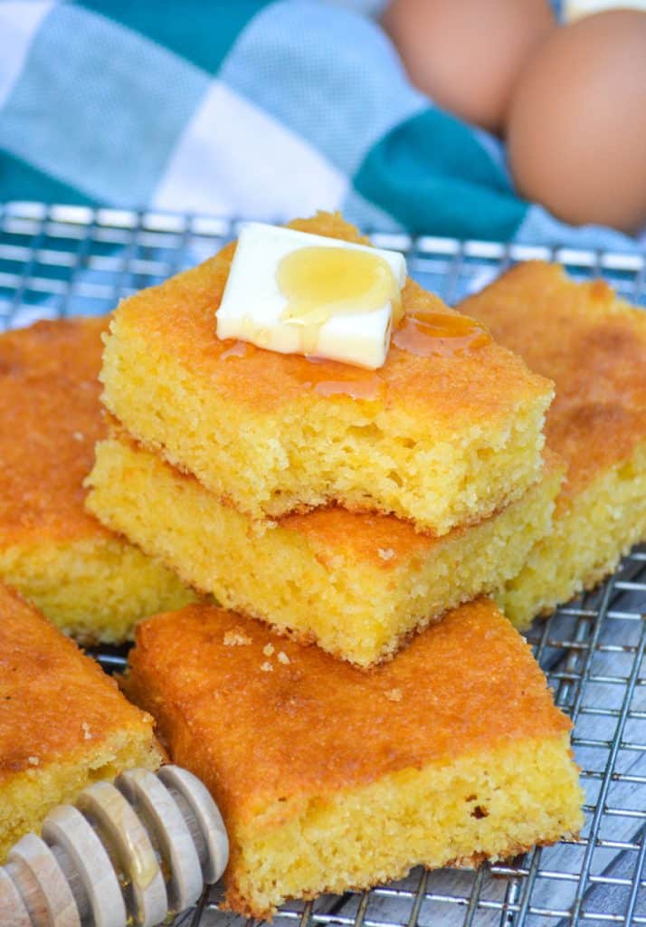slices of better cornbread from a box stacked on a wire cooling rack with a pat of butter and drizzle of honey on top