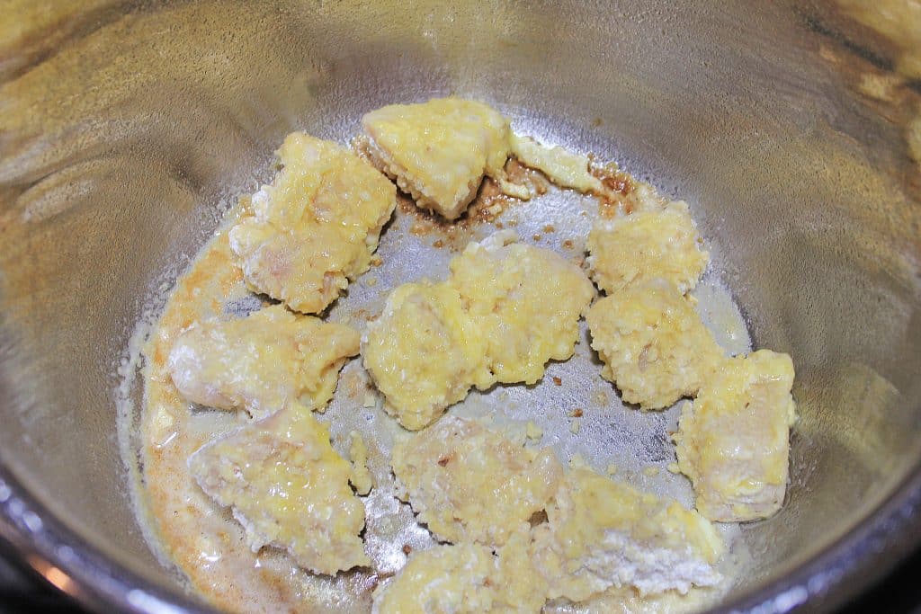 cornstarch coated chunks of chicken cooking in oil in the liner of an Instant Pot