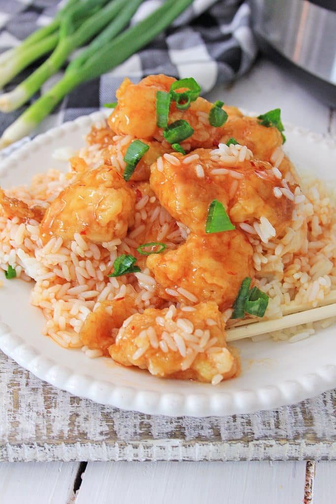 Instant pot sweet and sour chicken on a white plate with a pair of wooden chop sticks