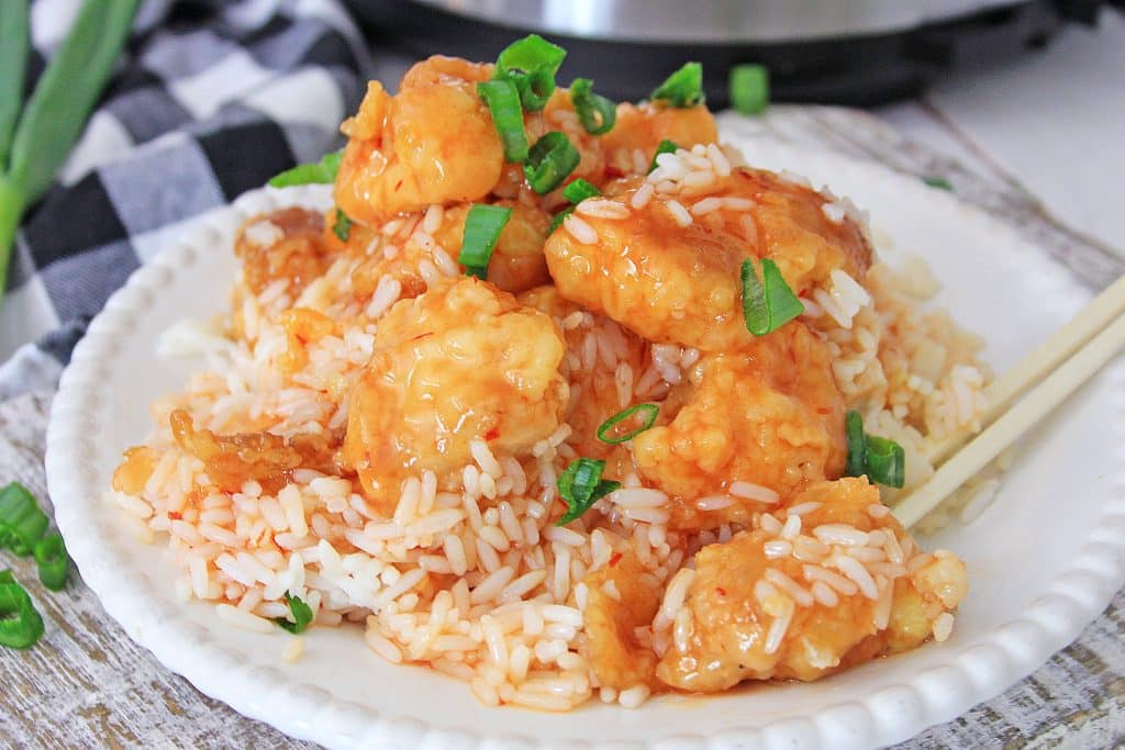 Instant pot sweet and sour chicken on a white plate with a pair of wooden chop sticks
