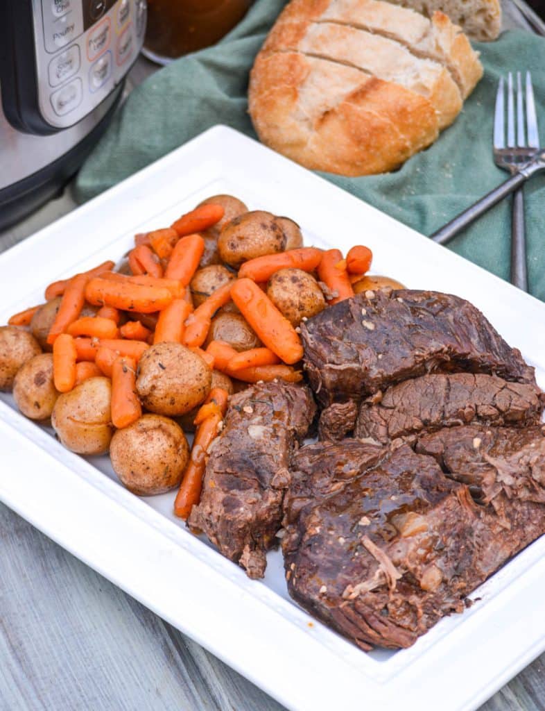 Instant Pot pot roast with carrots & potatoes arranged together on a white serving platter