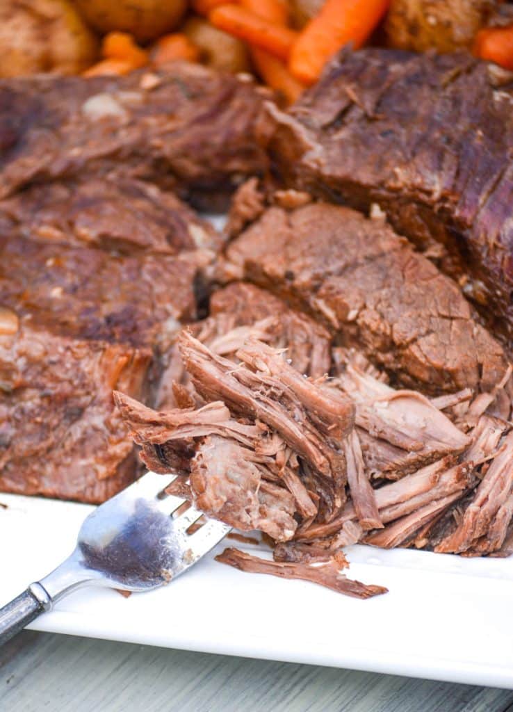 a fork with shredded beef on the edge of a white serving platter