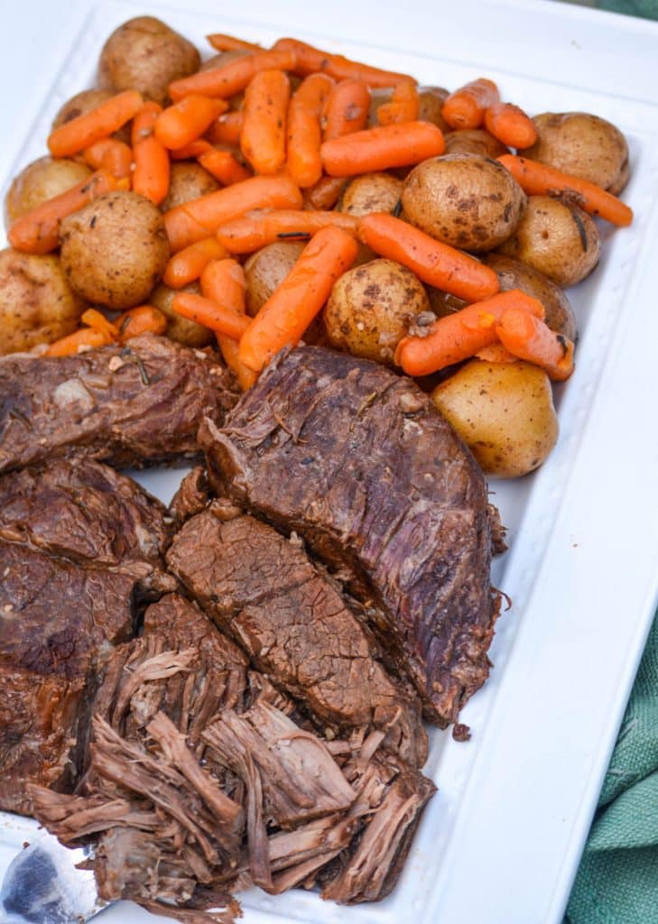 Instant Pot pot roast with carrots & potatoes arranged together on a white serving platter