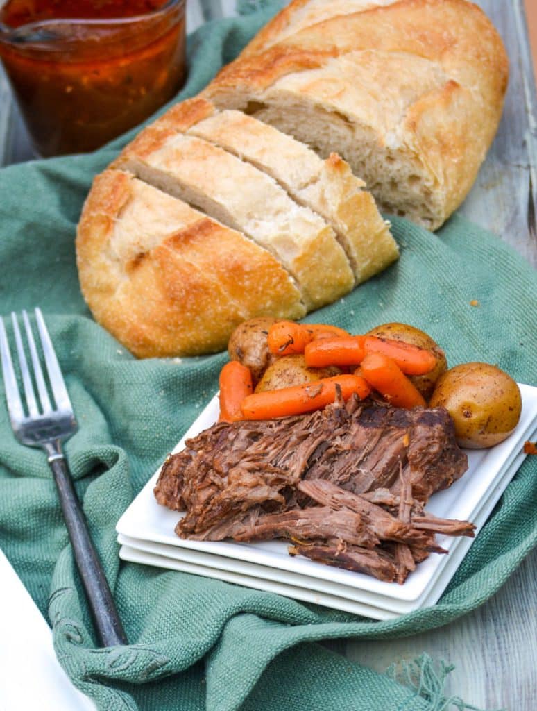 Instant Pot roast with potatoes & carrots served on a small white plate with bread and a fork in the background