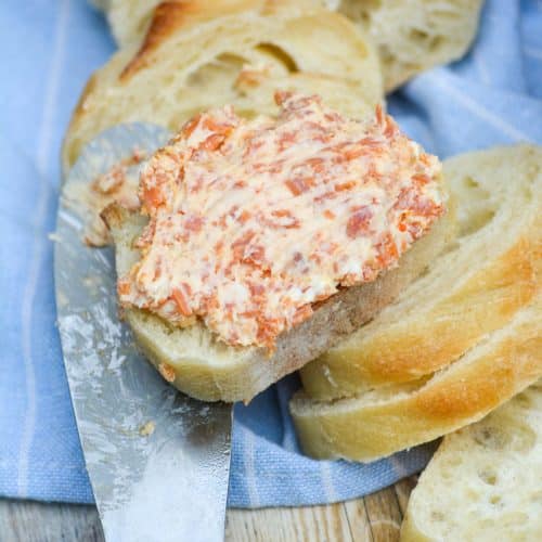 pepperoni pizza cream cheese spread smoothed over a baguette slice resting on a wooden handled cheese spreader