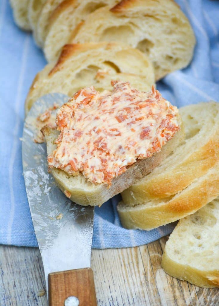 pepperoni pizza cream cheese spread smoothed over a baguette slice resting on a wooden handled cheese spreader