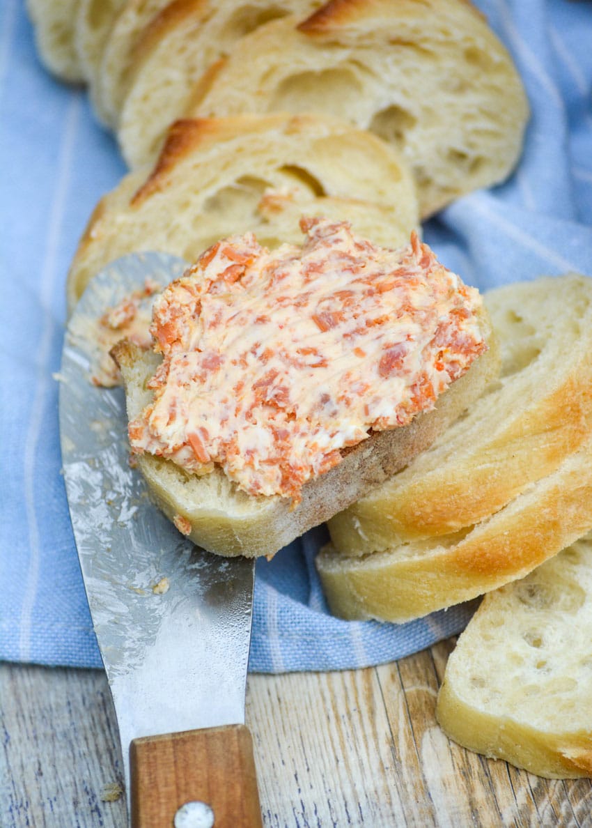pepperoni pizza cream cheese spread smoothed over a baguette slice resting on a wooden handled cheese spreader