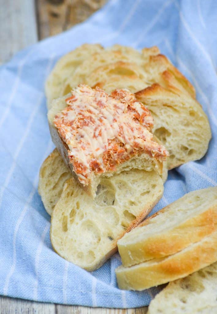 a bite taken out of a baguette slice topped with a layer of pepperoni cream cheese spread