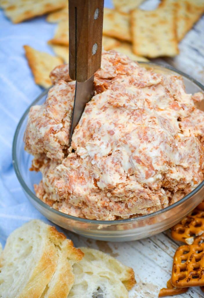 pepperoni cream cheese spread in a glass bowl with a wooden handled spreader stuck in the middle