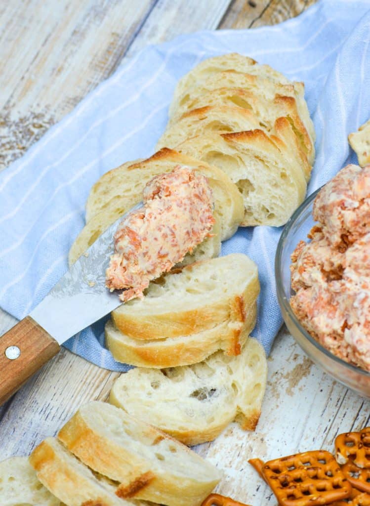 a spreader topped with pepperoni cream cheese resting on baguette slices