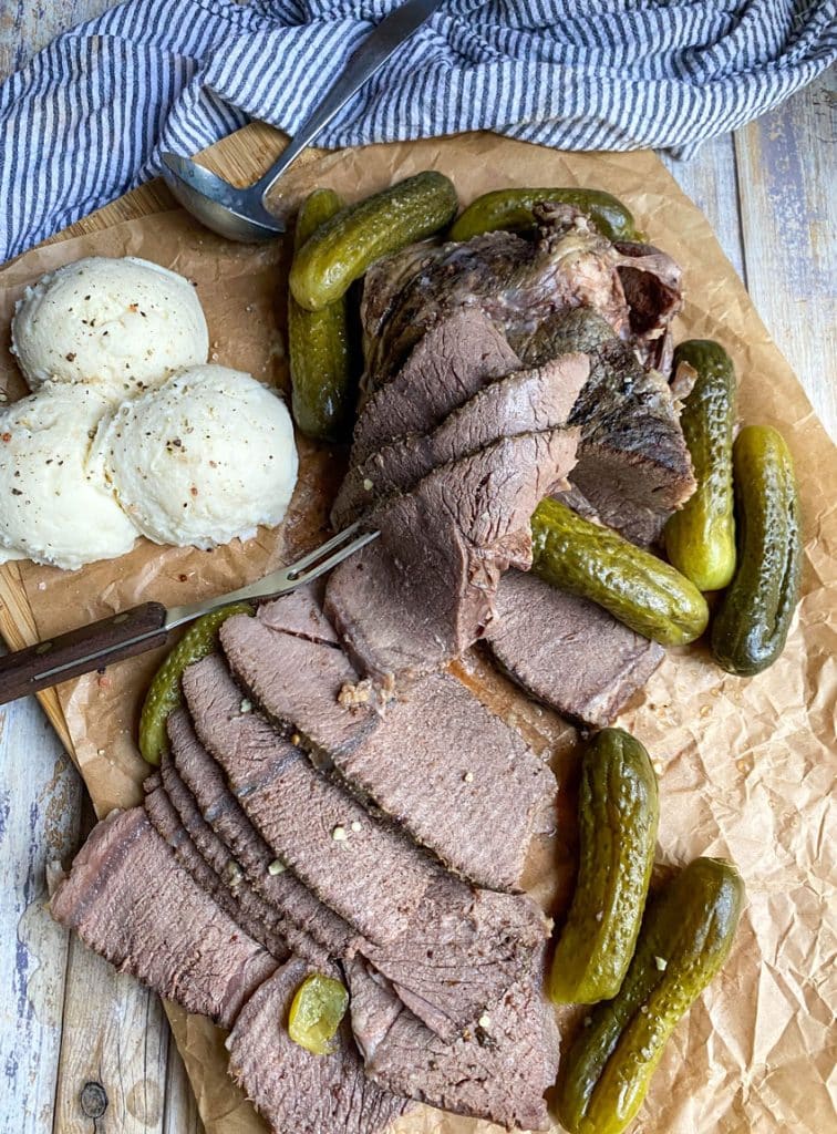 sliced slow cooker dill pickle pot roast with a meat fork on a parchment paper lined cutting board