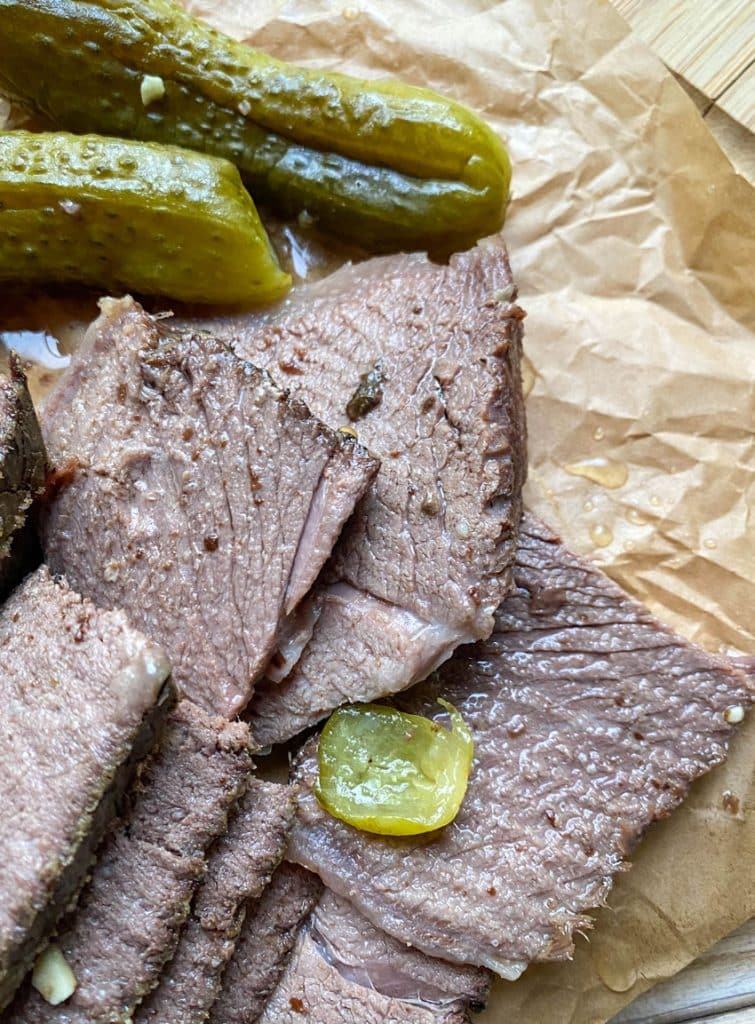 sliced slow cooker dill pickle pot roast with a meat fork on a parchment paper lined cutting board