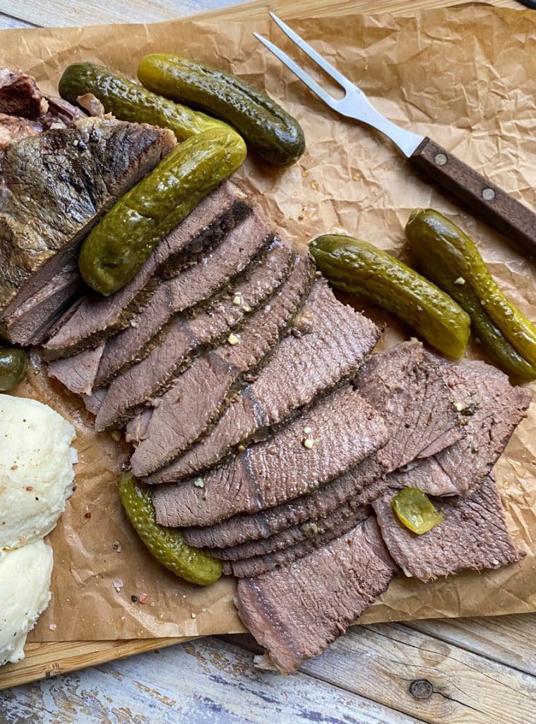 sliced slow cooker dill pickle pot roast with a meat fork on a parchment paper lined cutting board