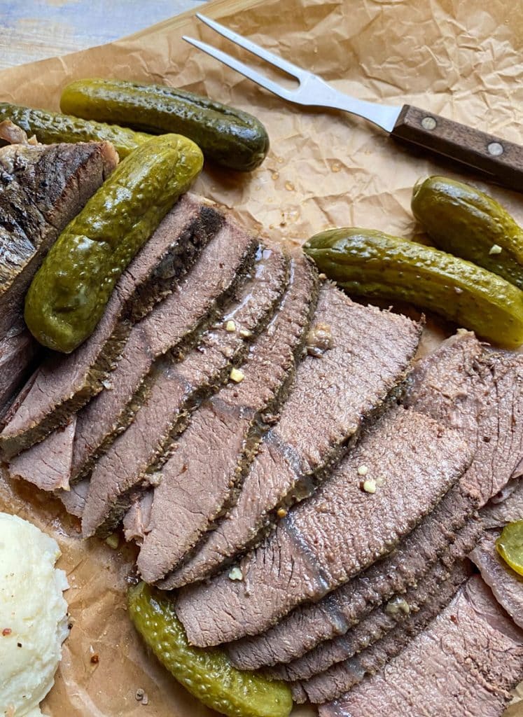 sliced slow cooker dill pickle pot roast with a meat fork on a parchment paper lined cutting board
