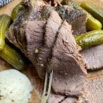 sliced slow cooker dill pickle pot roast with a meat fork on a parchment paper lined cutting board