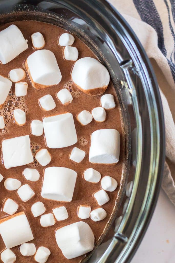 slow cooker peanut butter hot chocolate topped with marshmallows in a black crockpot