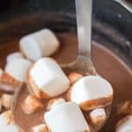 a silver ladle holding up a scoop of peanut butter hot chocolate with white marshmallows floating in it