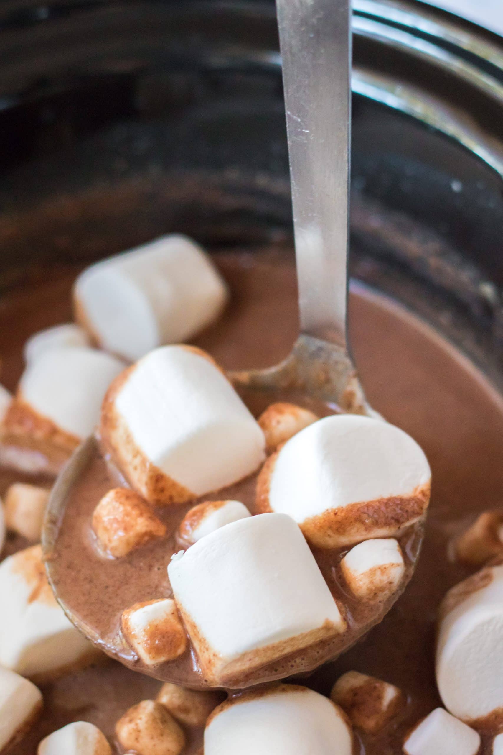 a silver ladle holding up a scoop of peanut butter hot chocolate with white marshmallows floating in it