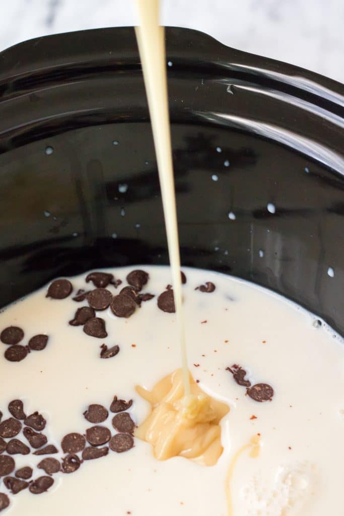 sweetened condensed milk being poured into a black crockpot